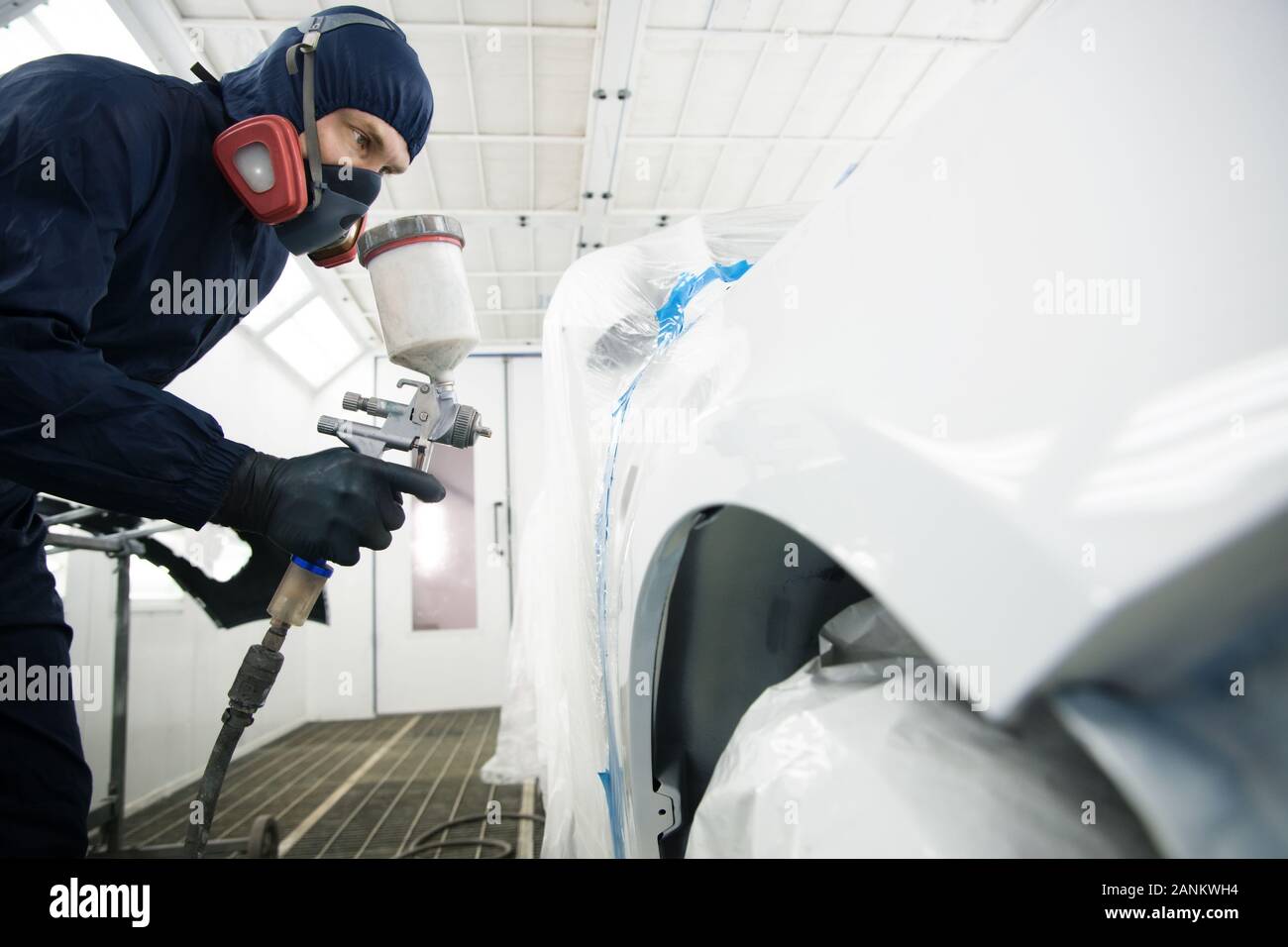 worker in overalls with a respirator and spray gun in his hand in the