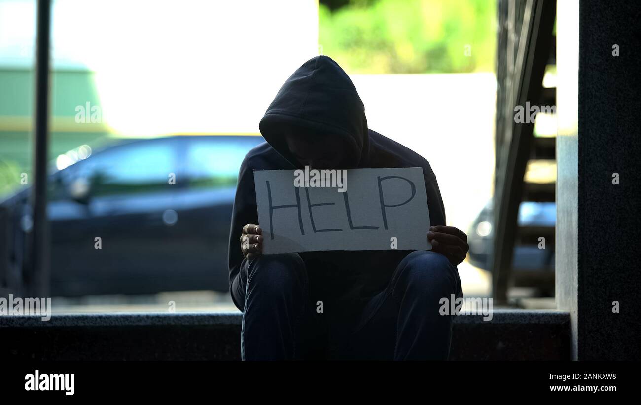 African-american teenager holding help cardboard sign, asking for alms in street Stock Photo