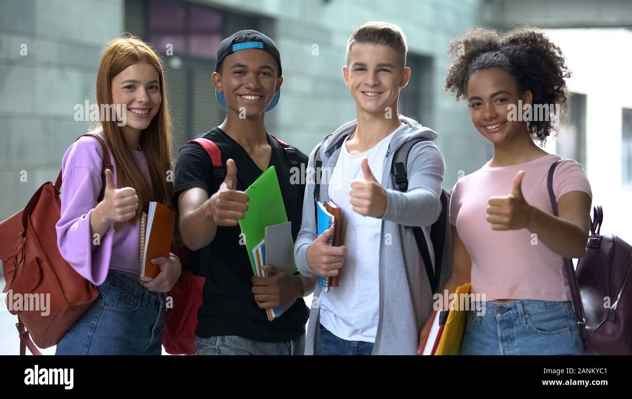 Smiling multiethnic students with notebooks showing thumbs up, college choice Stock Photo
