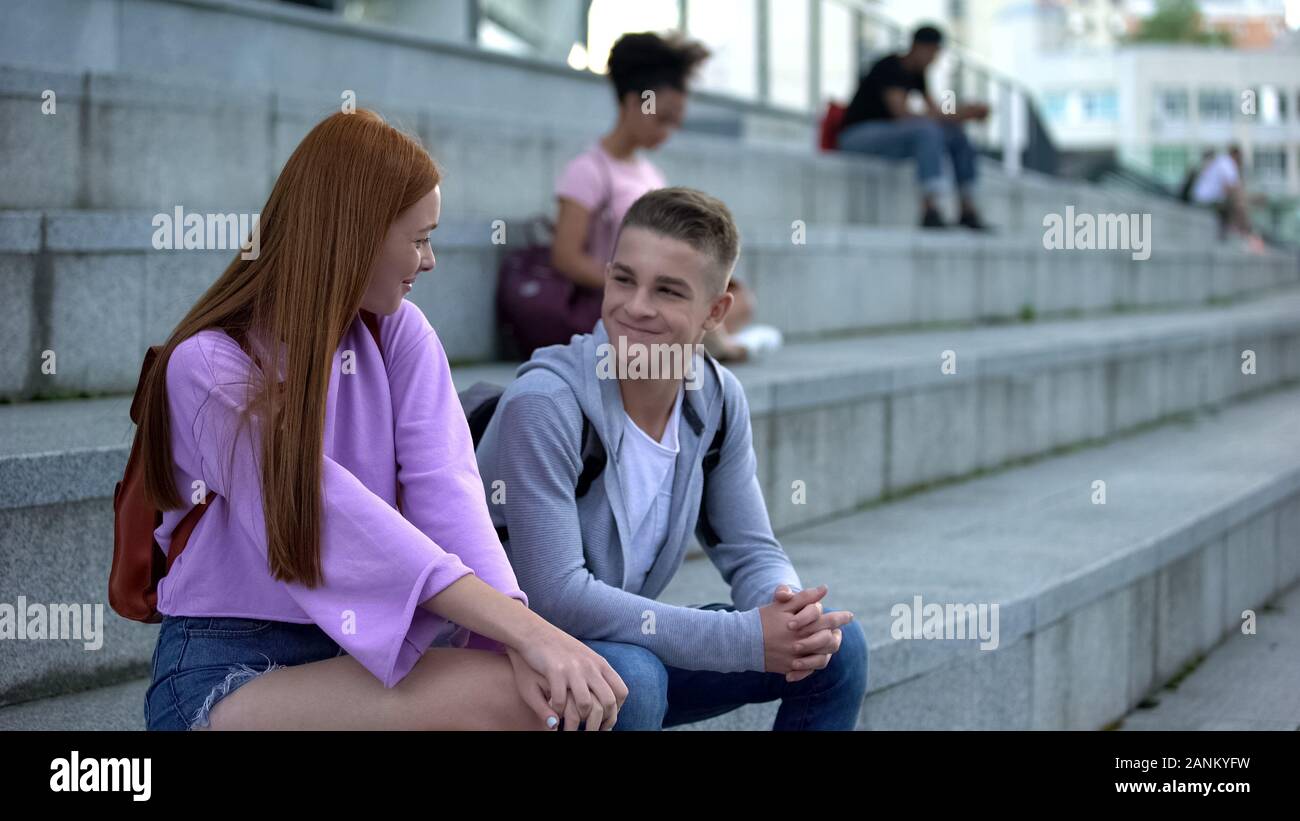 Beautiful redhead girl getting acquainted male teenager on campus stairs, flirt Stock Photo
