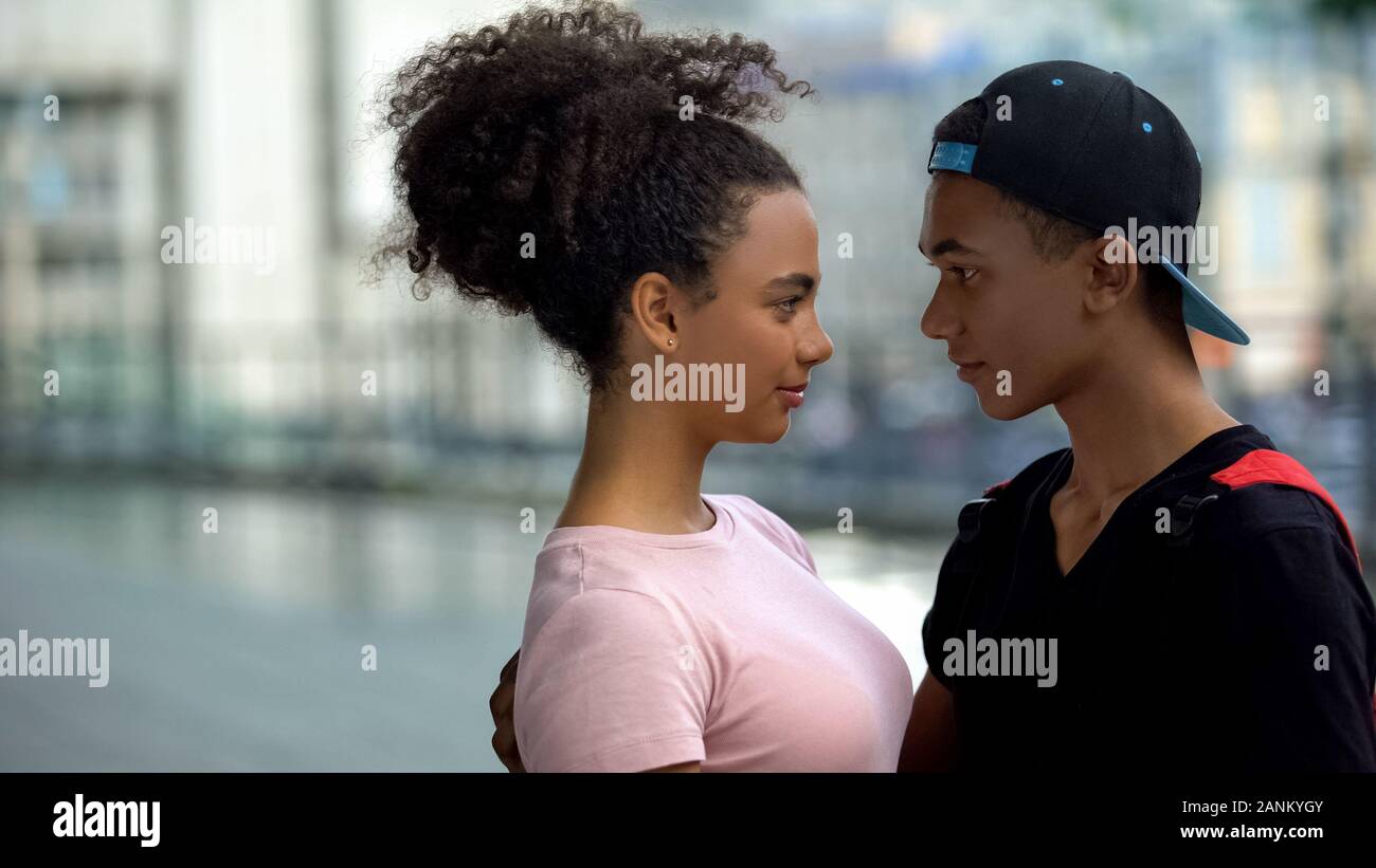 Mixed-race couple of teens embracing and looking each other, romantic date Stock Photo