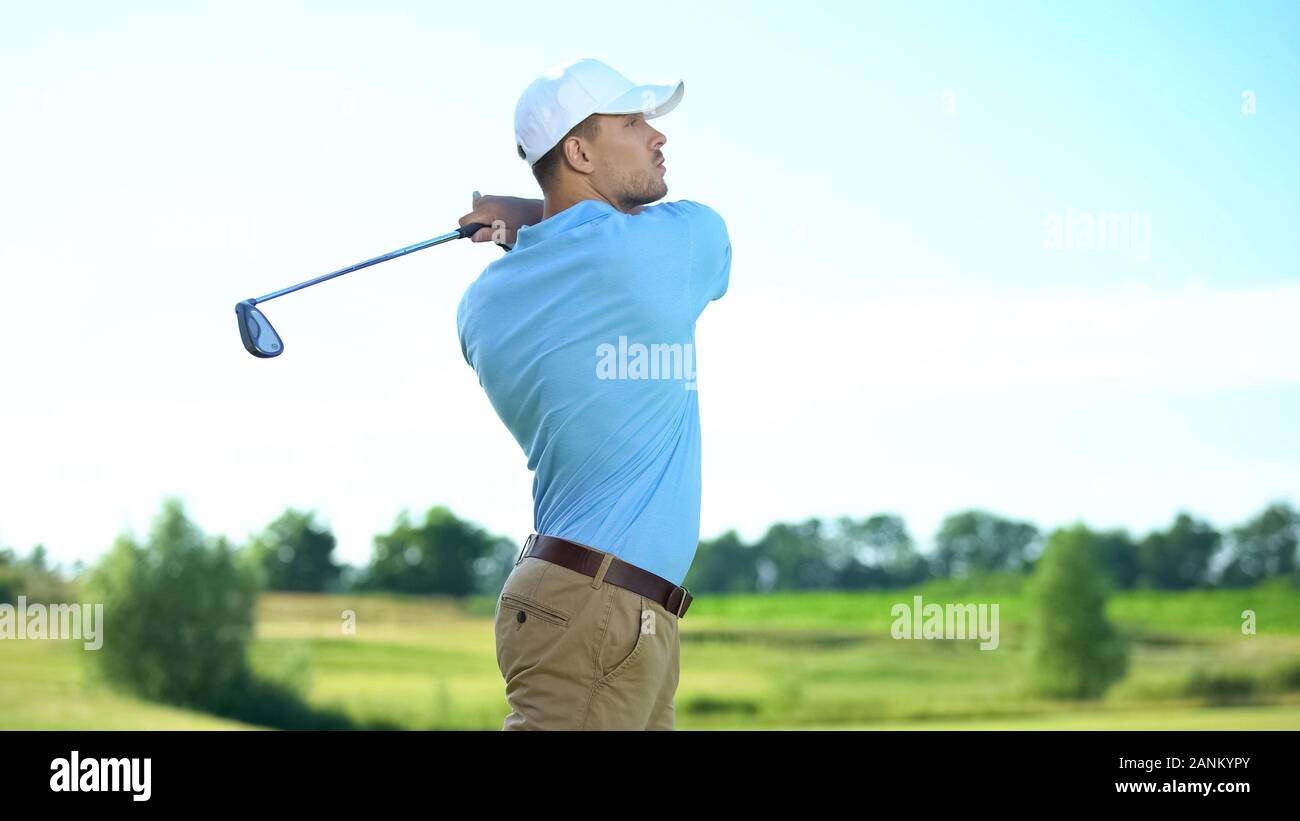 Professional golfer hitting ball in swing position, looking at meadow