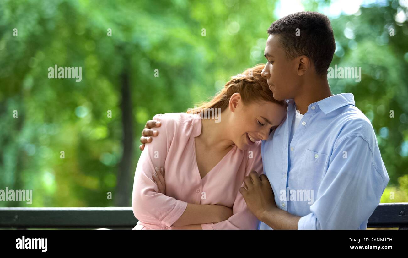 Afro-American teen boy hugging crying girlfriend in park, school problems Stock Photo