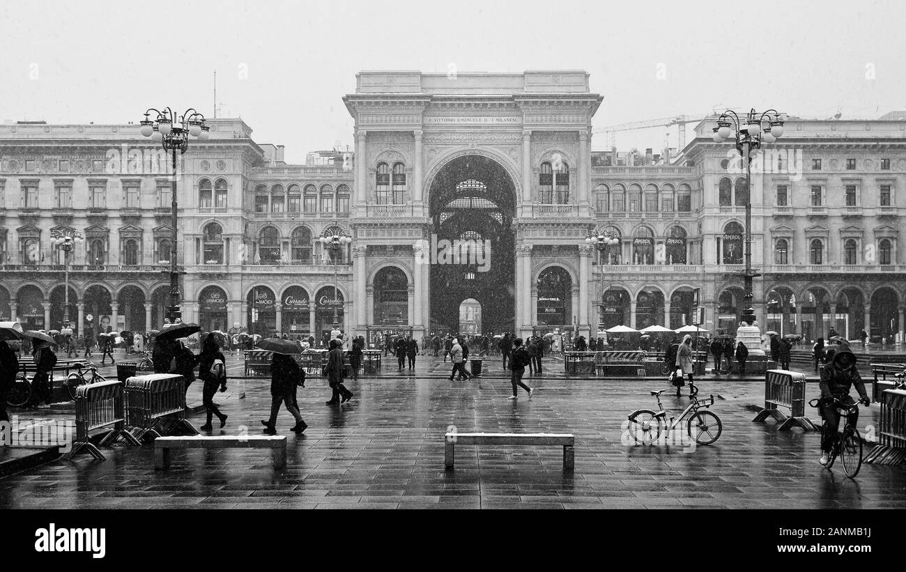 Piazza del Duomo with Galleria Vittorio Emanuele arcade and Palazzo dei Portici with people and bicycles while snowing - Milan, Italy (2018) Stock Photo