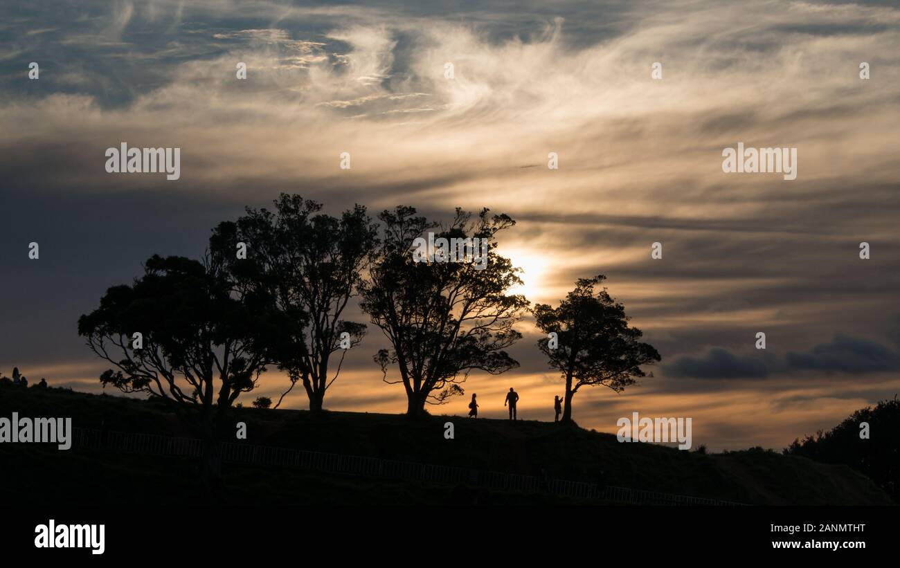 Silhouette image of people walking at the top of Mt Eden at Sunset, Auckland, New Zealand Stock Photo
