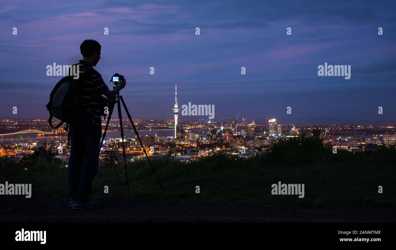 Photographer taking photos of Auckland city at sunset at the top of Mount Eden Stock Photo