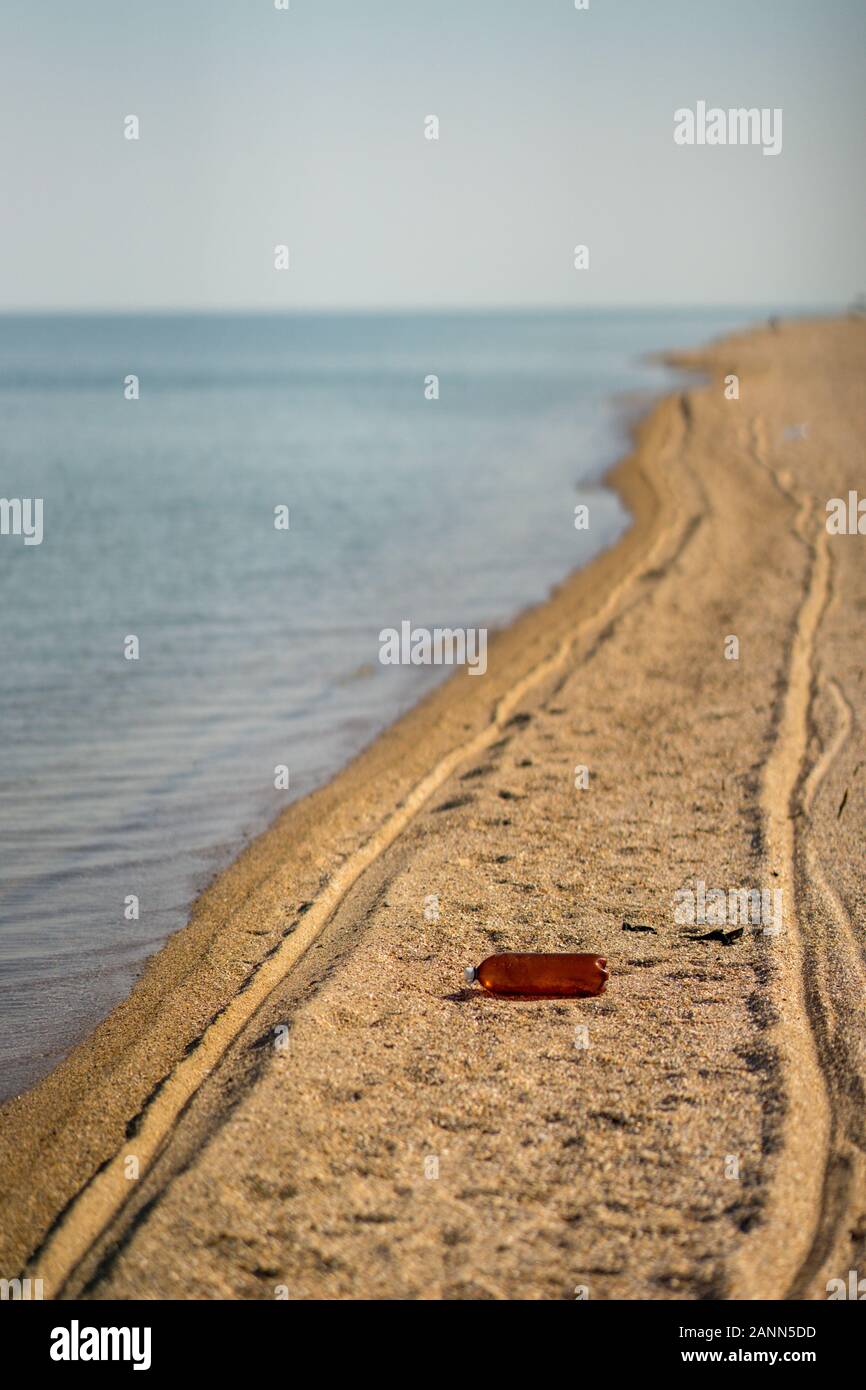 Empty plastic bottle lying on the beach. Environmental pollution. Tire tracks on the sand Stock Photo