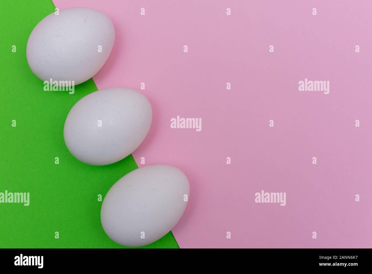 Three Easter holiday flat lay with white egg on a solid bright green, and light pink pastel background with copy space. Stock Photo