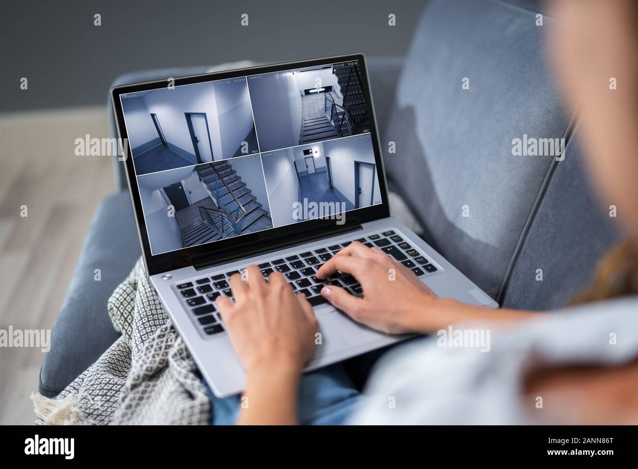 Close-up Of Woman Sitting On Couch Monitoring Home Security Cameras On Laptop At Home Stock Photo