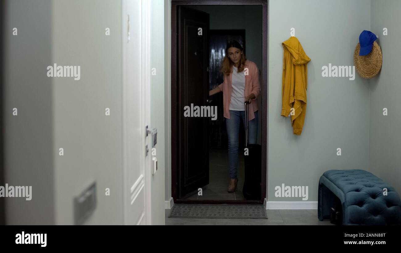 Woman with suitcase entering rent apartment, dreaming about own housing Stock Photo