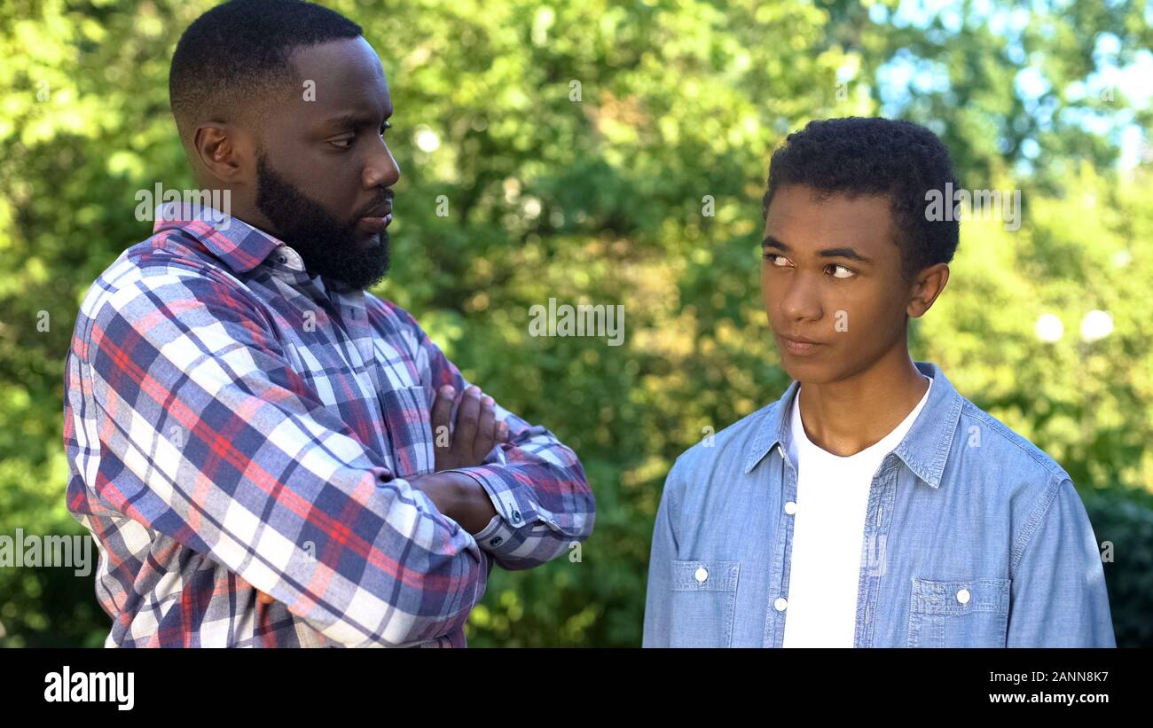 Strict black dad looking at guilty teenage son, upbringing methods, family Stock Photo