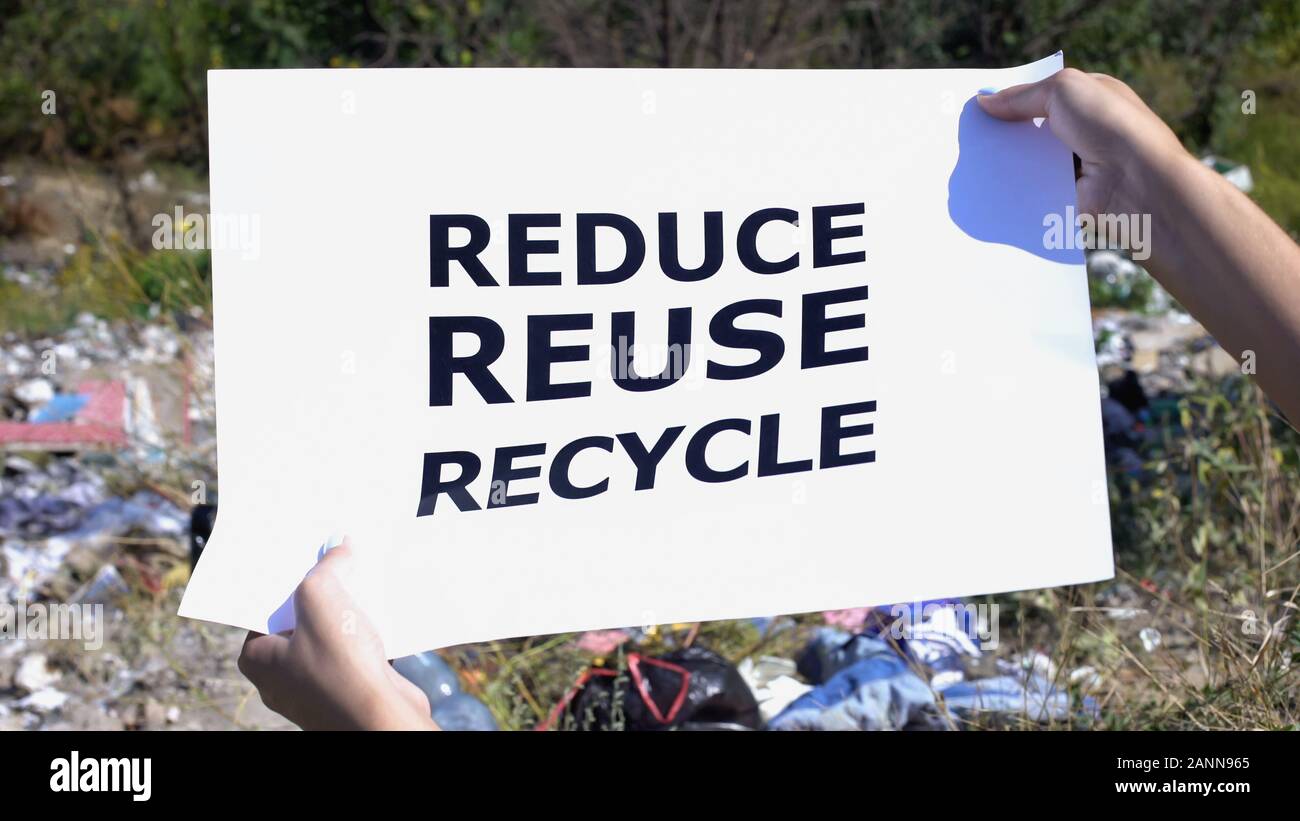 Reduce reuse recycle phrase on cardboard in hands against landfill ...