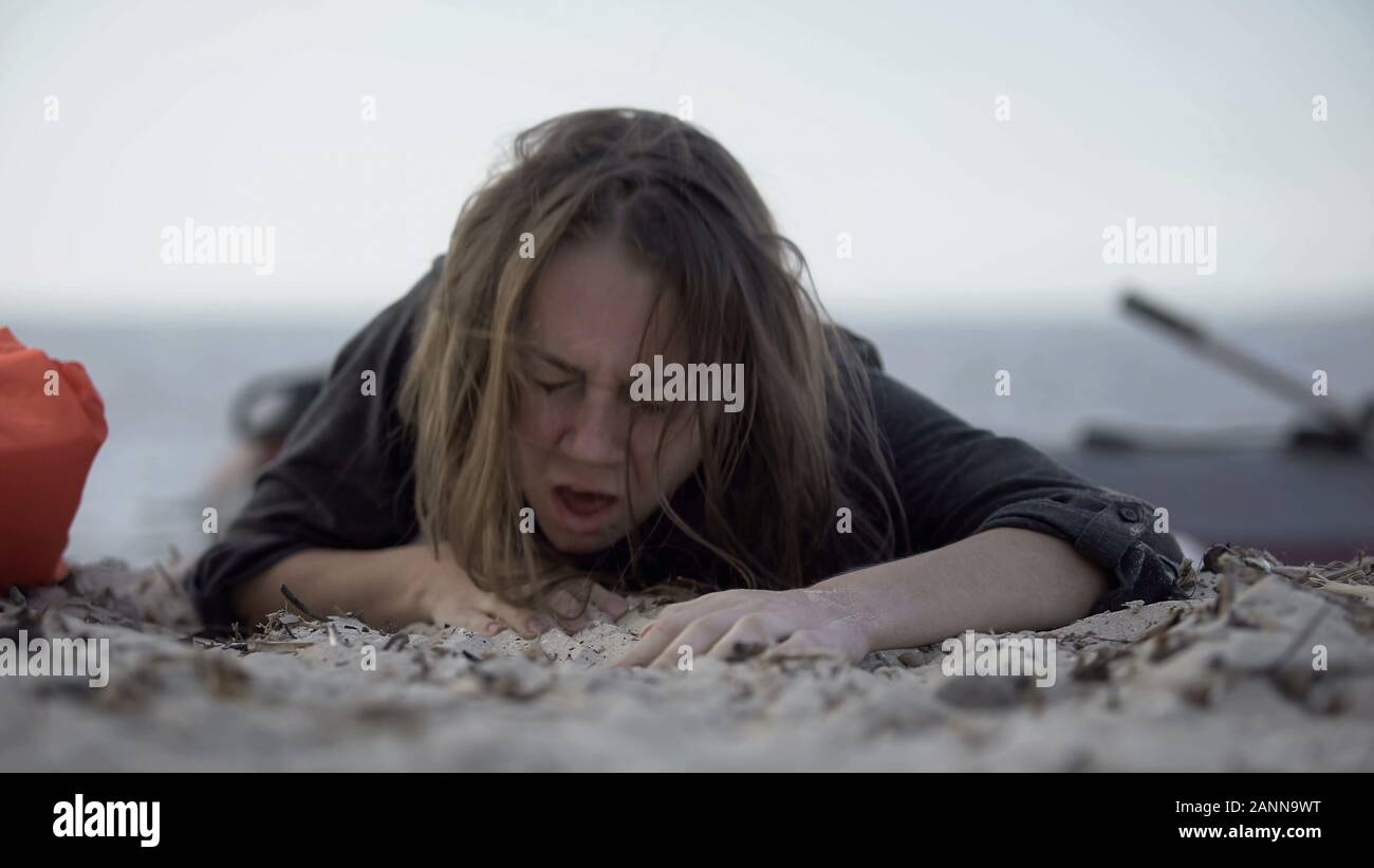 Woman coughing, trying to crawl on sand, surviving natural catastrophe, victim Stock Photo