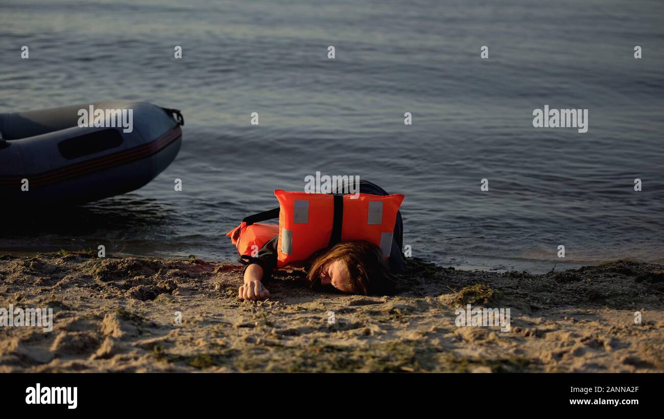 Woman in life jacket lying on shore near boat, victim of shipwreck