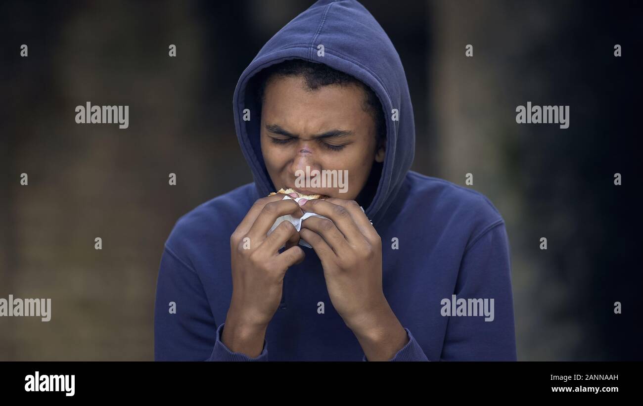 Black young man with face scar eating snack street, troubled teen, behavior Stock Photo