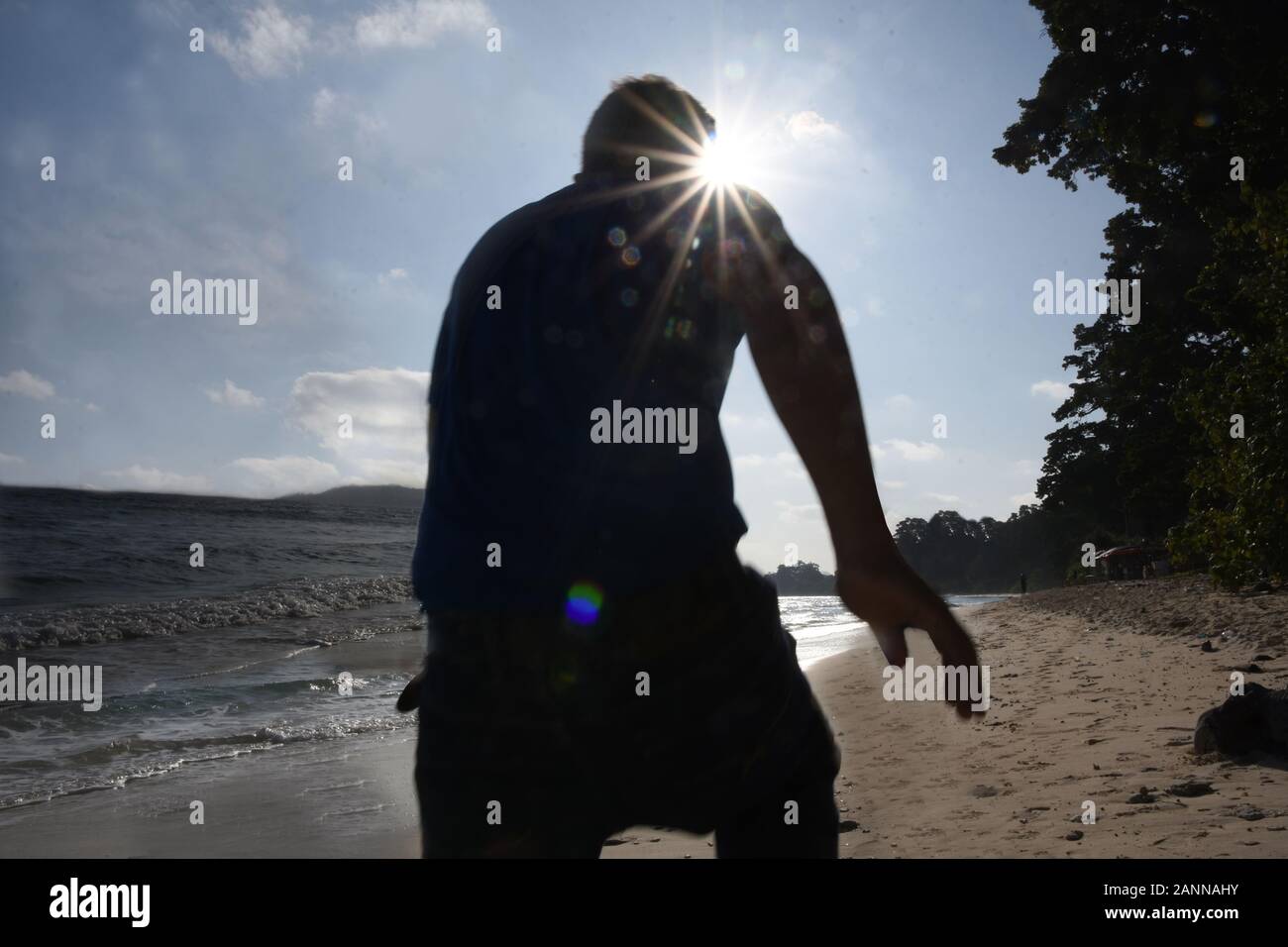 Silhouette Back view of man running on beach , Photographed with HDR view of Sea and Cloud along with sun as star shape at Neil Island Stock Photo