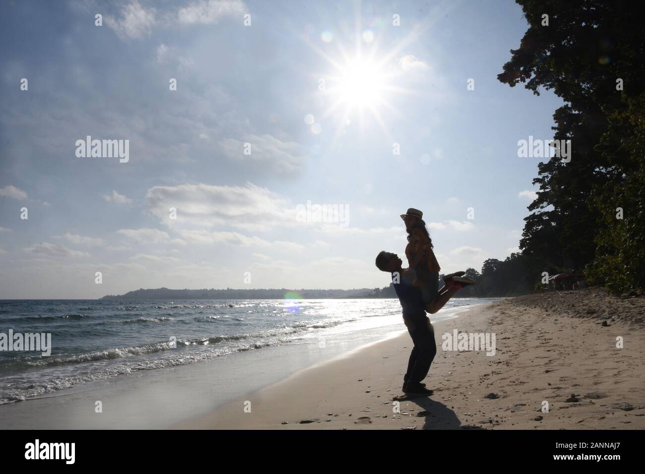 Silhouette of a young couple playing against the backdrop of the sun glare at the beach of Neil Island Stock Photo