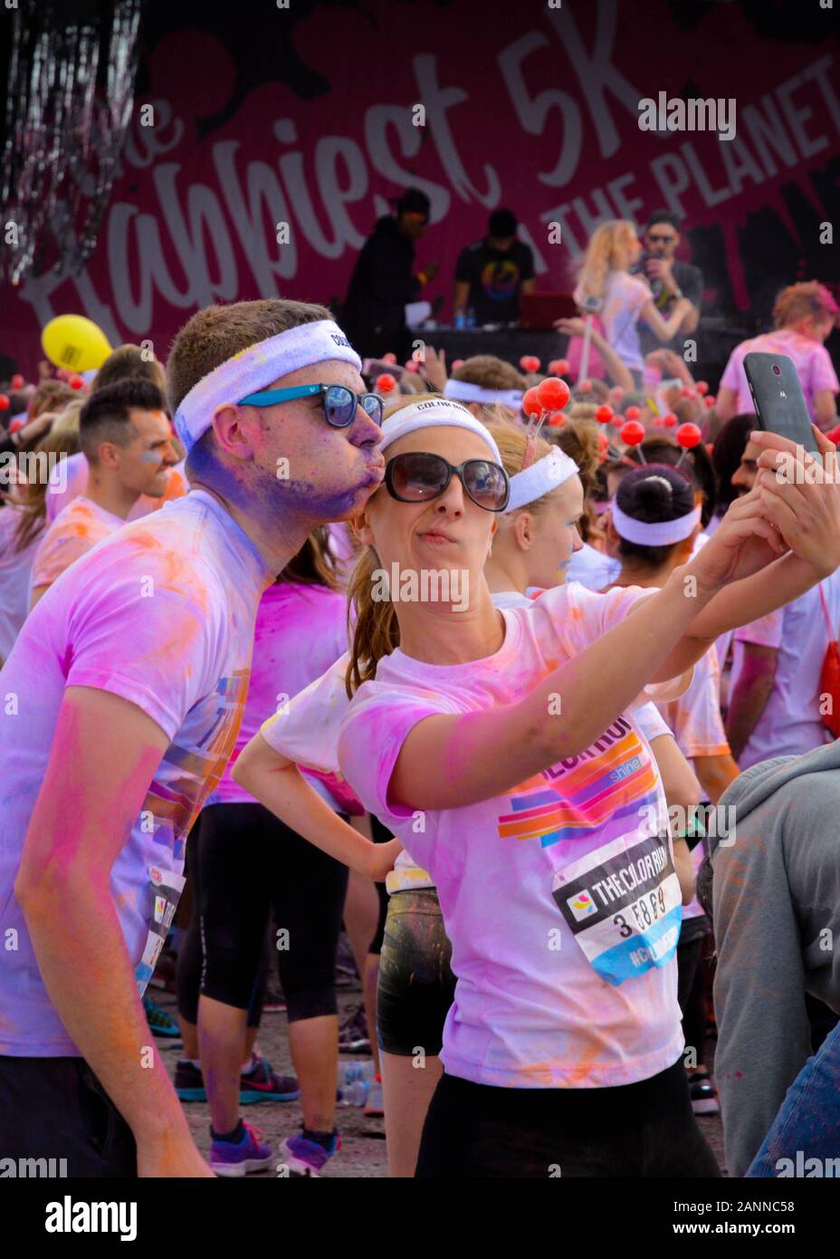 Man and woman celebrating completing The Color Run in Birmingham 2015 by taking a selfie on mobile phone whilst pulling silly facial expressions Stock Photo