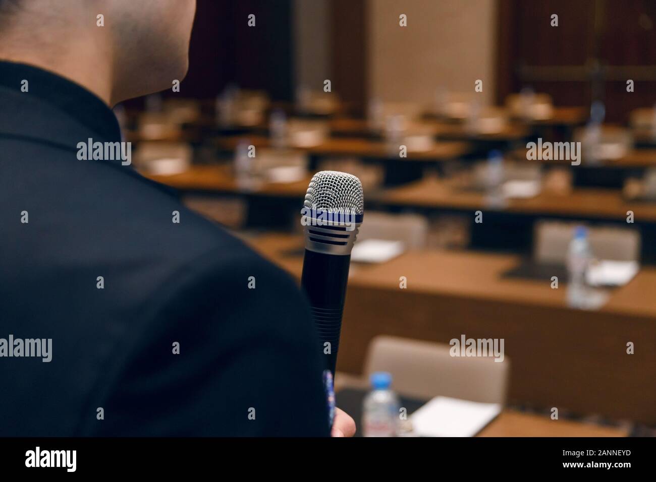 Microphone in hand of man in suit on background of empty conference hall. Rehearsal of public speaking Stock Photo