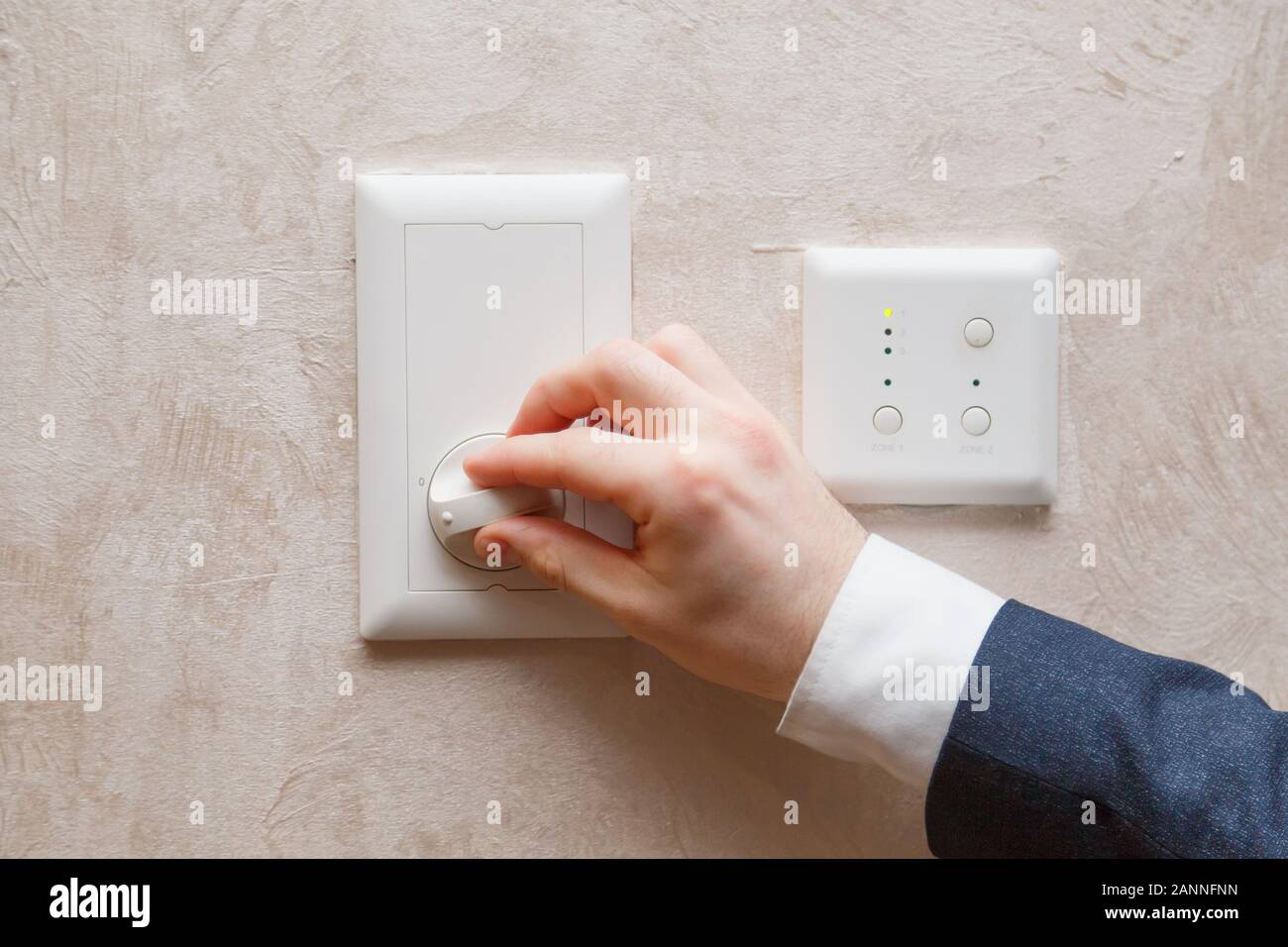 Man regulating temperature on air conditioning controller thermostat on the wall Stock Photo