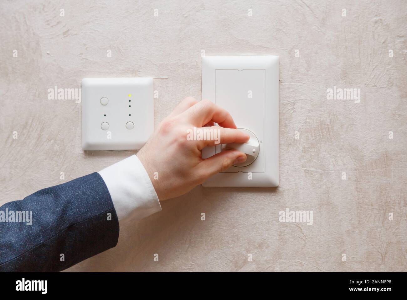 Man regulating temperature on air conditioning controller thermostat on the wall Stock Photo