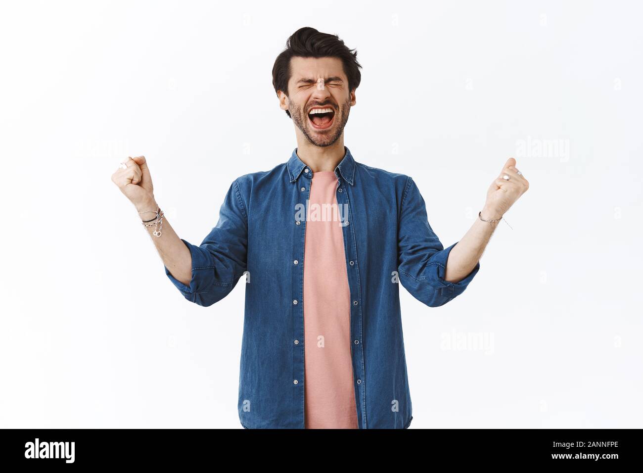 Joyful extremely happy handsome bearded guy yelling from happiness out loud, close eyes and clench fists, pump hands up from joy, winning feeling luck Stock Photo
