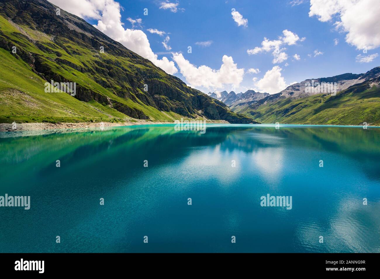Mountains reflect in the clear blue water of the mountain lake Lac de Moiry in the Pennine Alps on a summer day with a nice blue sky and some white cl Stock Photo