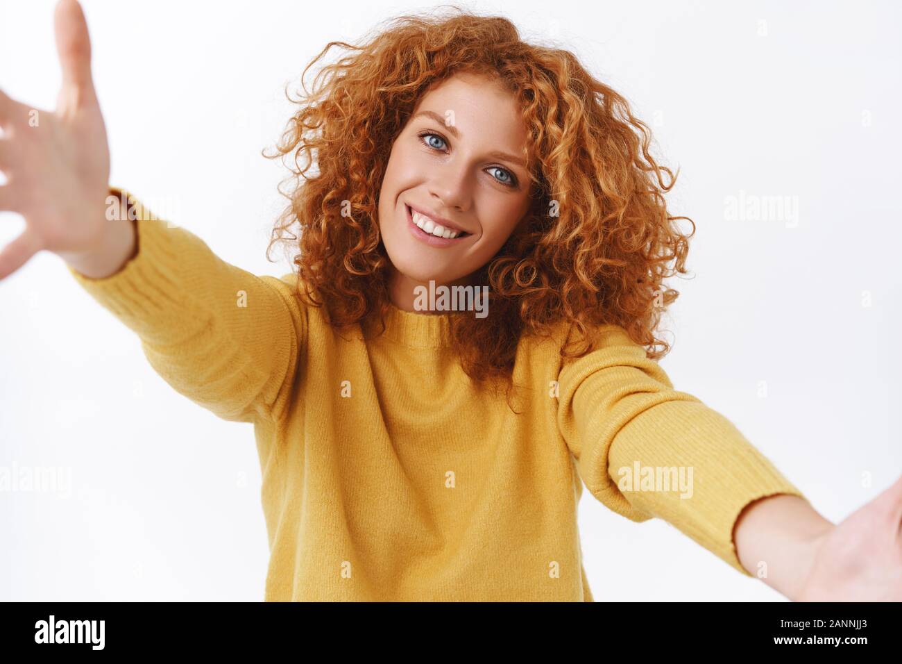 Close-up portrait, friendly and lovely, smiling happy curly redhead woman in yellow sweater, tilt head silly grinning, spread arms to hug friend tight Stock Photo
