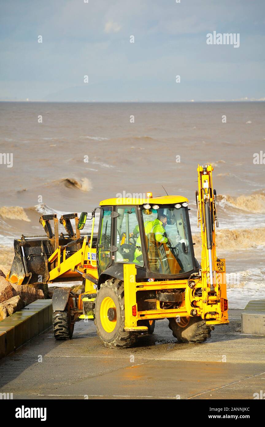 Yellow JCB excavator working on Fleetwood seafront at high tide on a stormy day Stock Photo