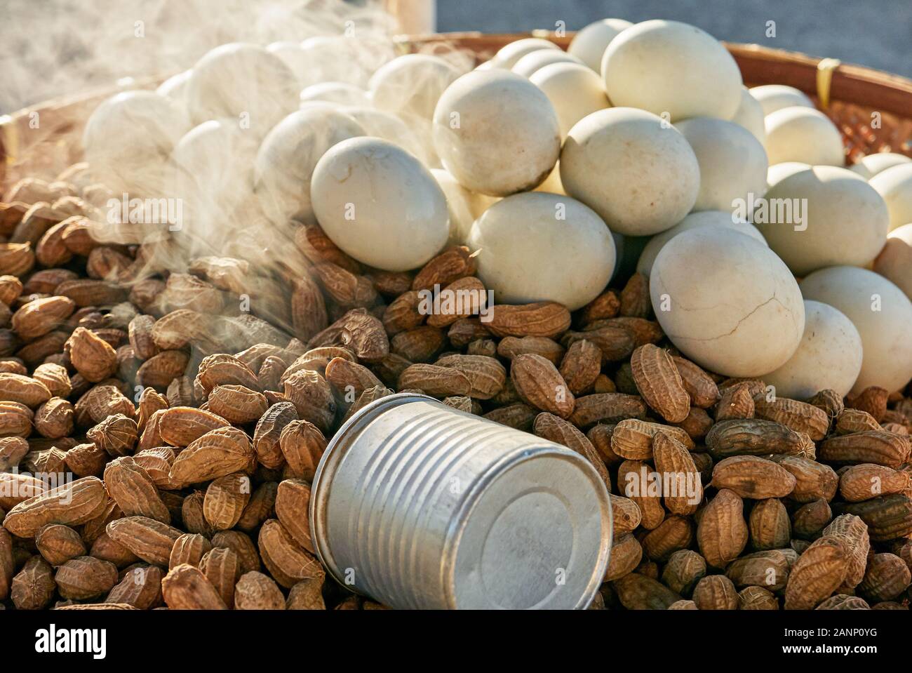 Close-up of steamed peanuts and white boiled eggs for sale on a native bamboo tray with a measuring cup, seen in the Philippines at late afternoon Stock Photo