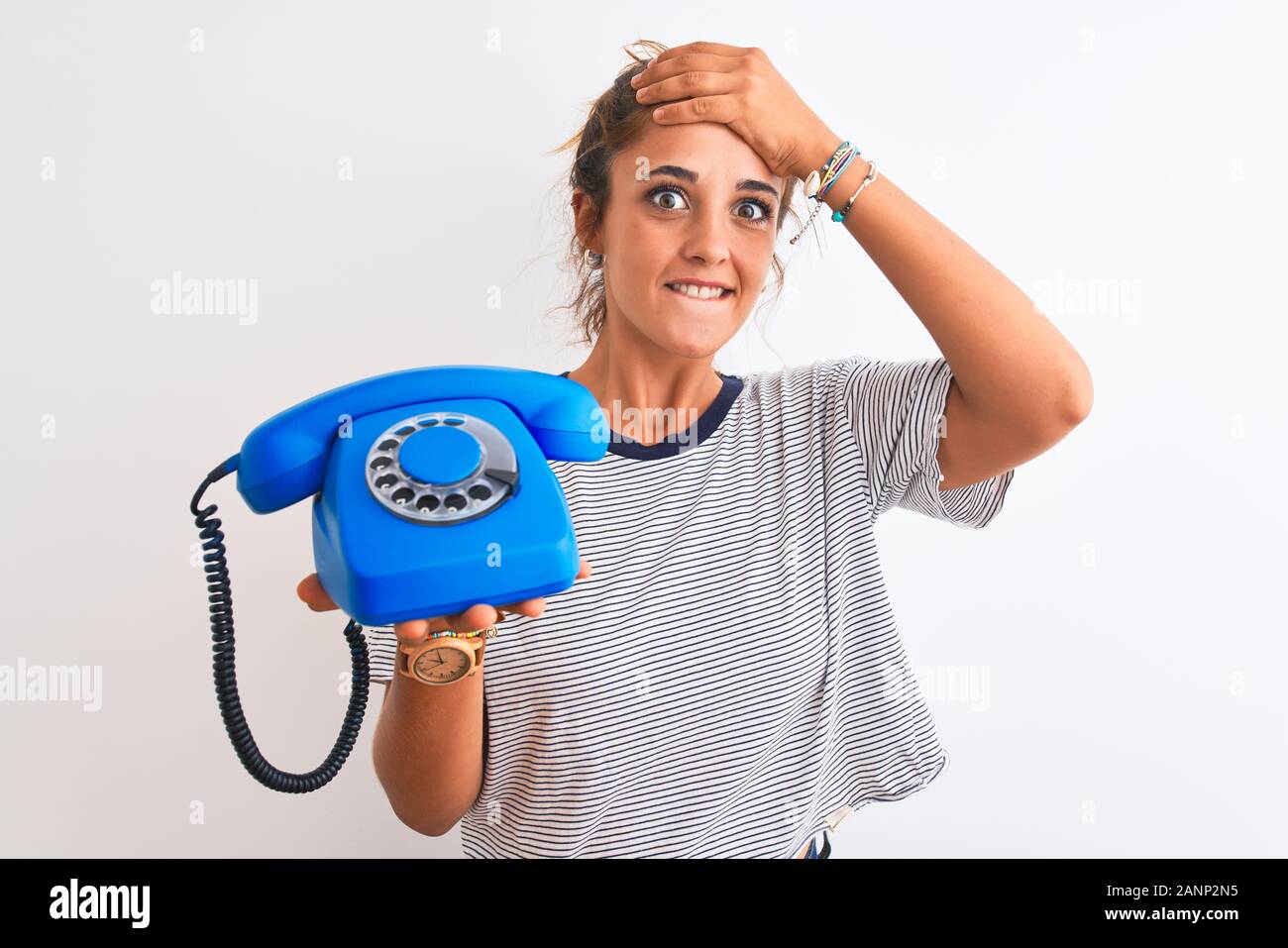 Young redhead woman holding classic retro telephone over isolated background stressed with hand on head, shocked with shame and surprise face, angry a Stock Photo