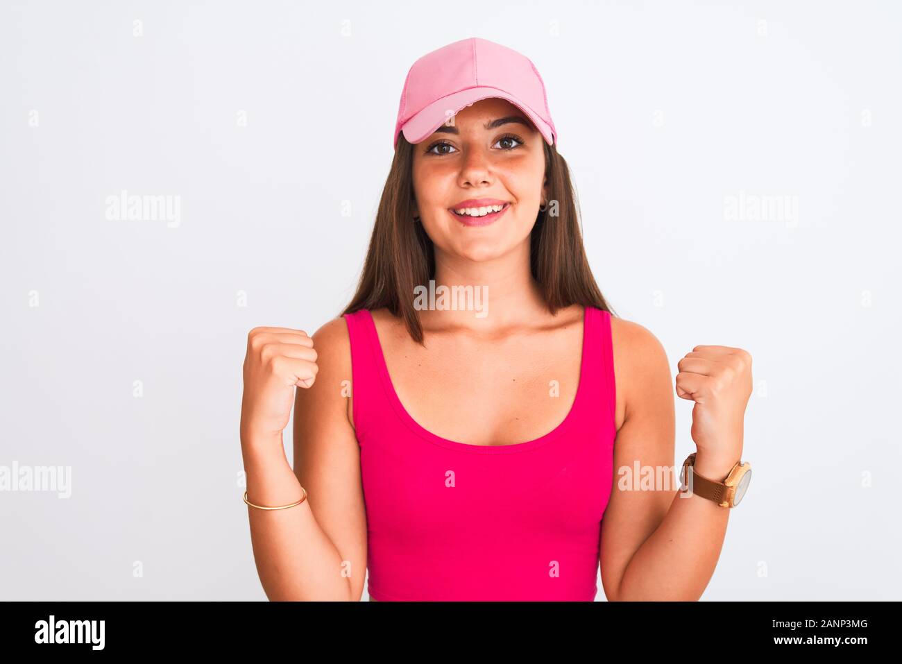 Young beautiful girl wearing pink casual t-shirt and cap over isolated white background celebrating surprised and amazed for success with arms raised Stock Photo