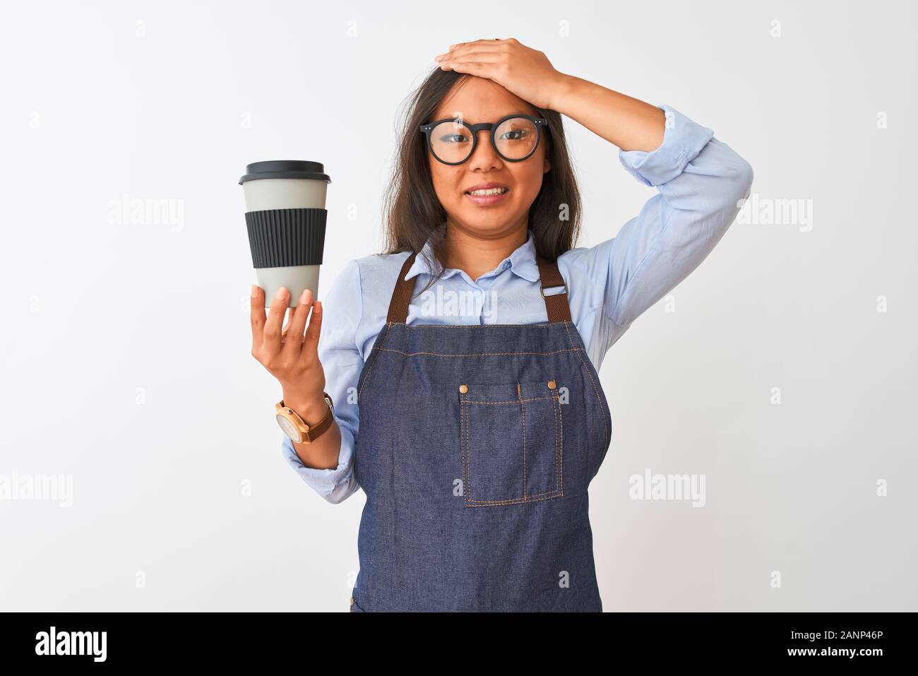 Young chinese barista woman wearing glasses holding coffee over isolated white background stressed with hand on head, shocked with shame and surprise Stock Photo