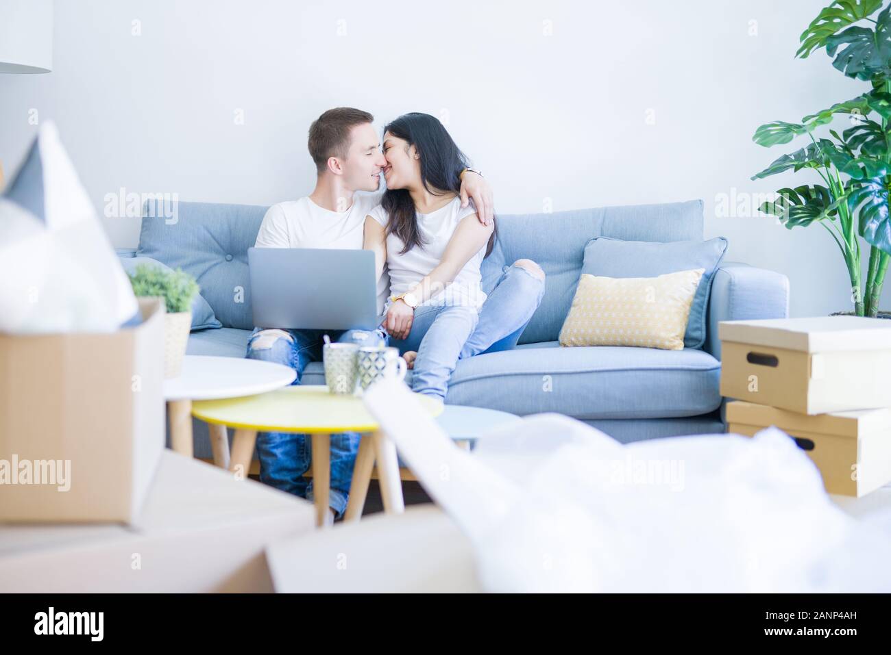 Young beautiful couple sitting on the sofa using laptop at new home ...