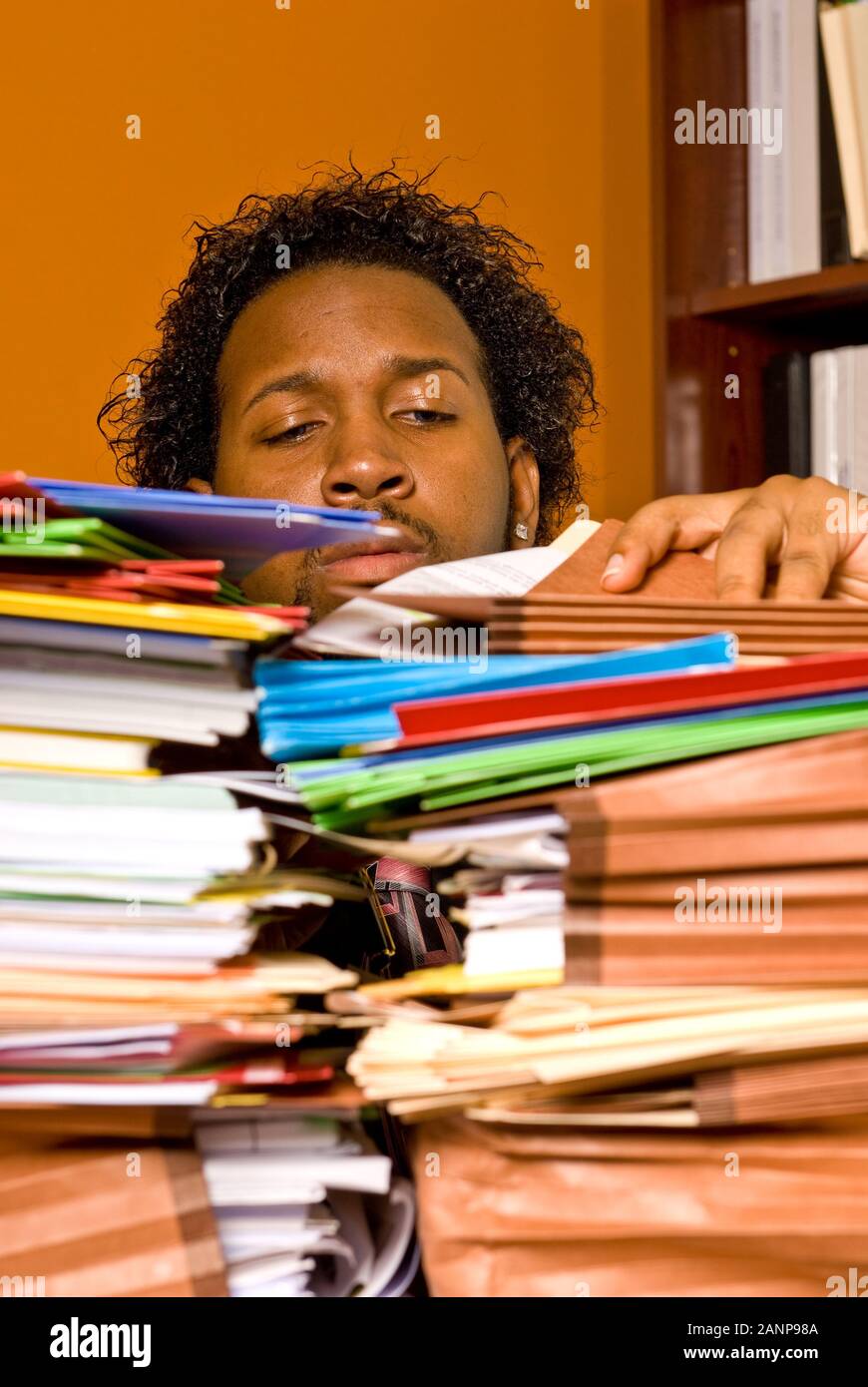 Over worked young man looking through a pile of colorful folders on his desk Stock Photo