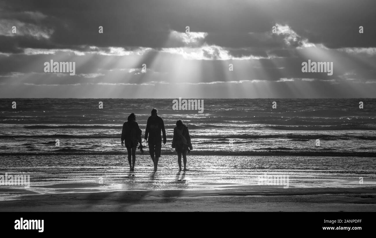 Black and white photo of three people walking at the Piha beach, west Auckland, New Zealand Stock Photo