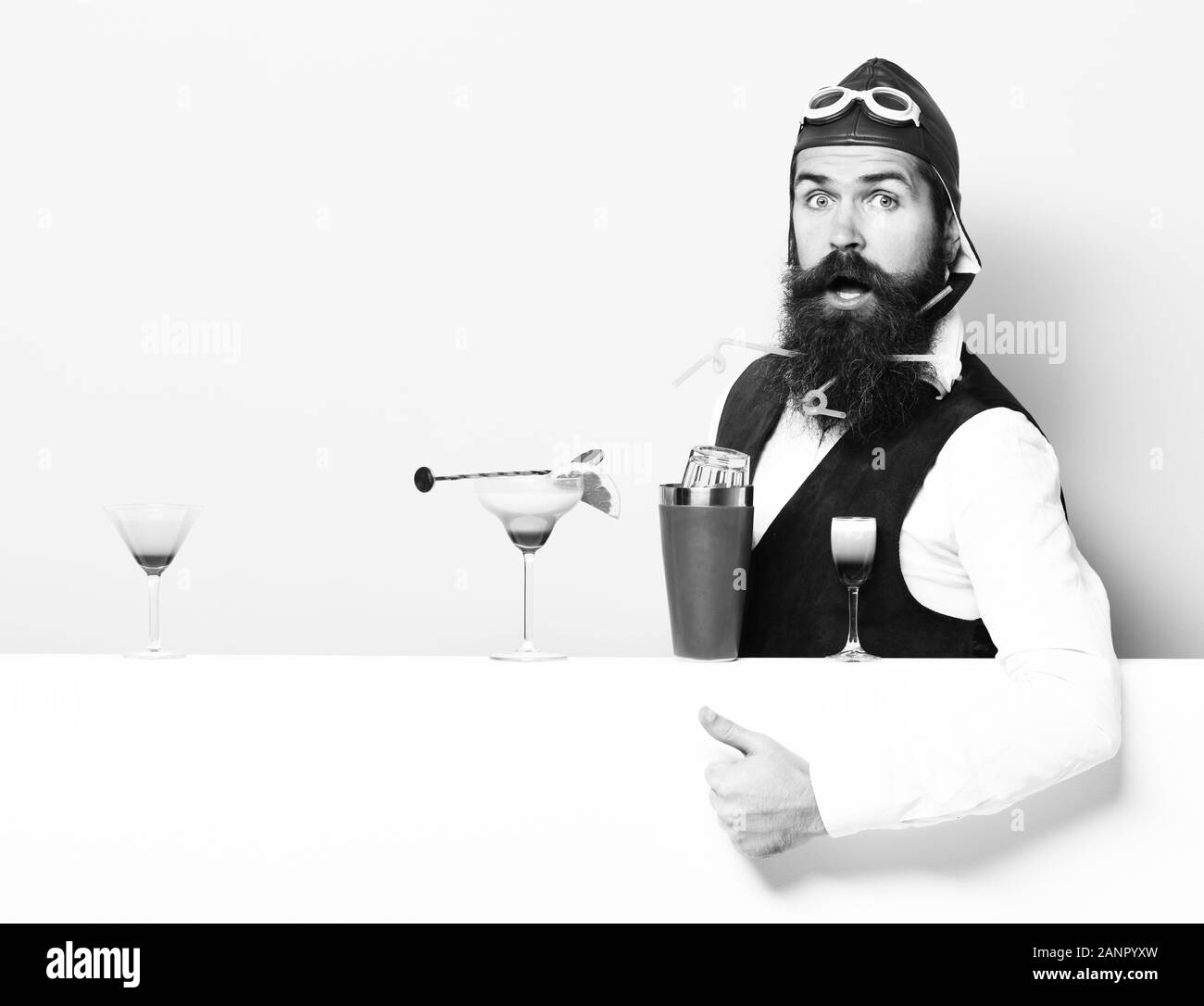 handsome bearded aviator or pilot with beard and mustache on surprised face with shaker alcoholic cocktails in vintage suede leather waistcoat with hand, and glasses on purple green studio background Stock Photo