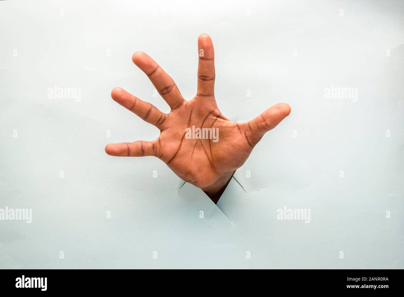 black person hand through a hole in a cardboard with open palm spread out showing all five