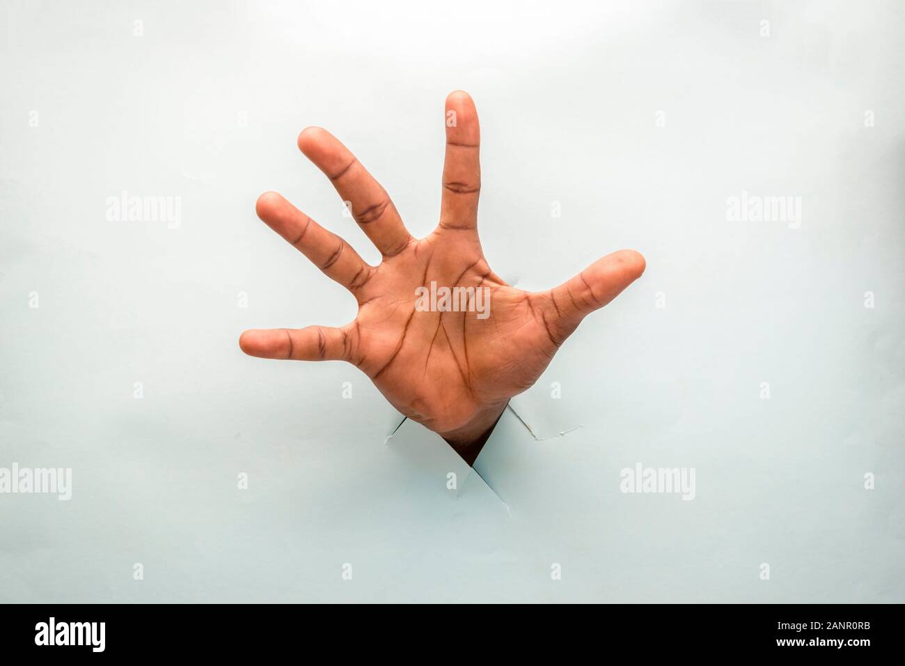 black hand through a hole in a cardboard with open palm spread out