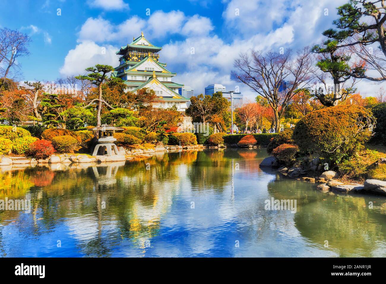 Beautiful Osaka castle in the middle of green autumnal garden with pond reflecting colours of traditional japanese architecture and blue sky. Stock Photo