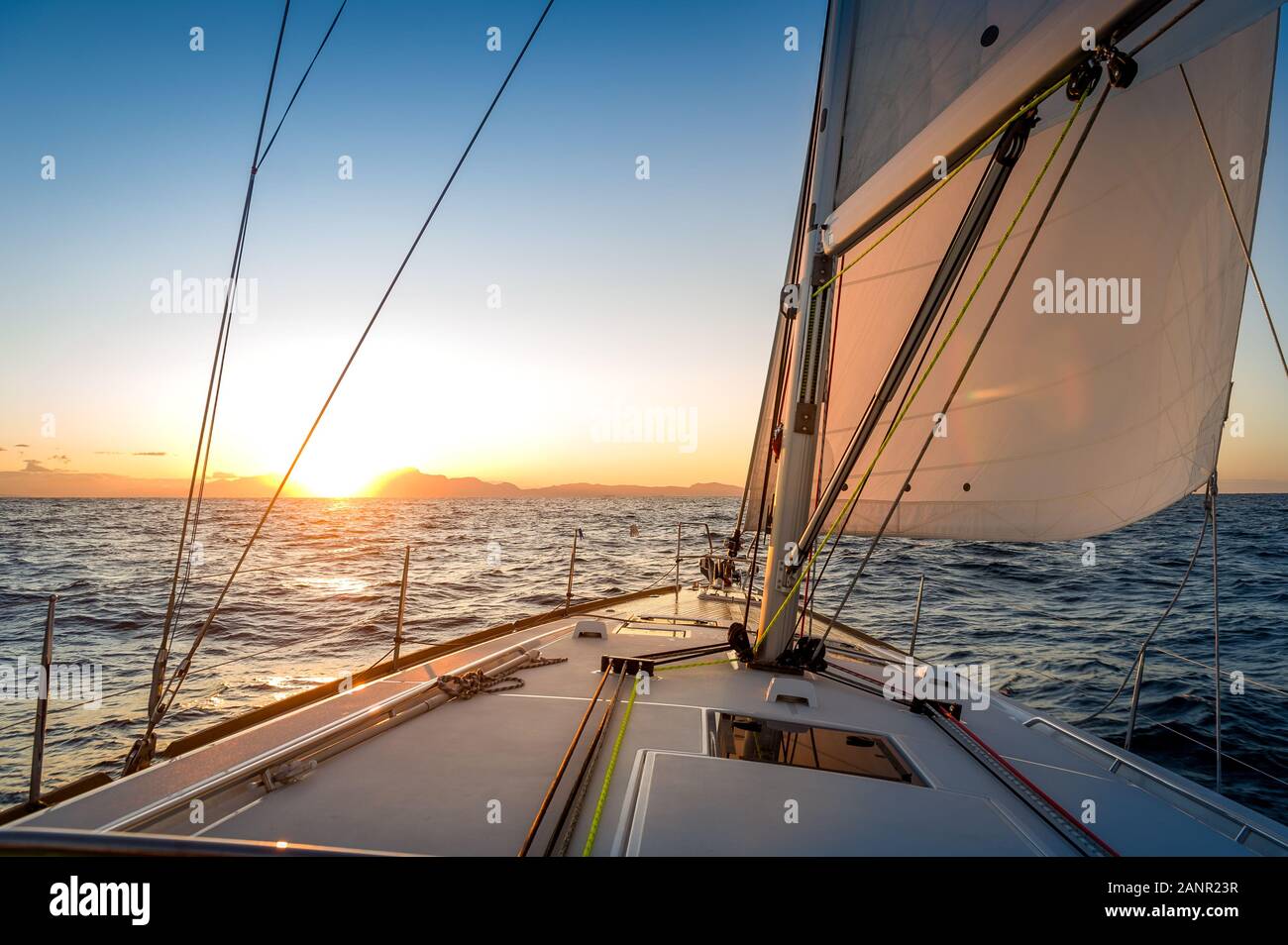 Chasing the sun at sailing yacht. Deck and sails of sailoat pointing to the sunrise. Mediterranean sea, Italy. Stock Photo