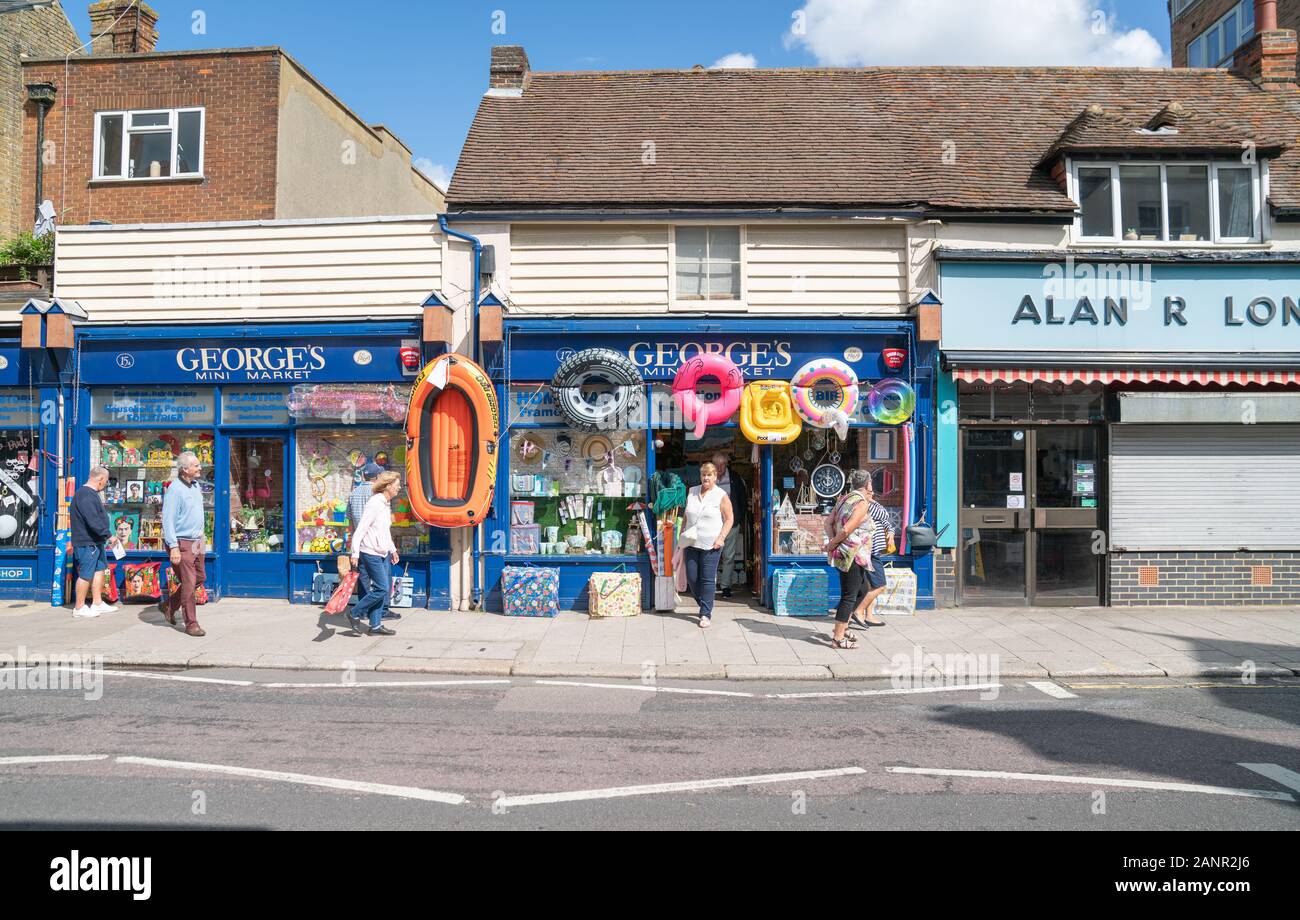 Whitstable England - August 18 2019; People passing Georges Mini Market with beach toys inflatable rings and boat displayed on High Street. Stock Photo