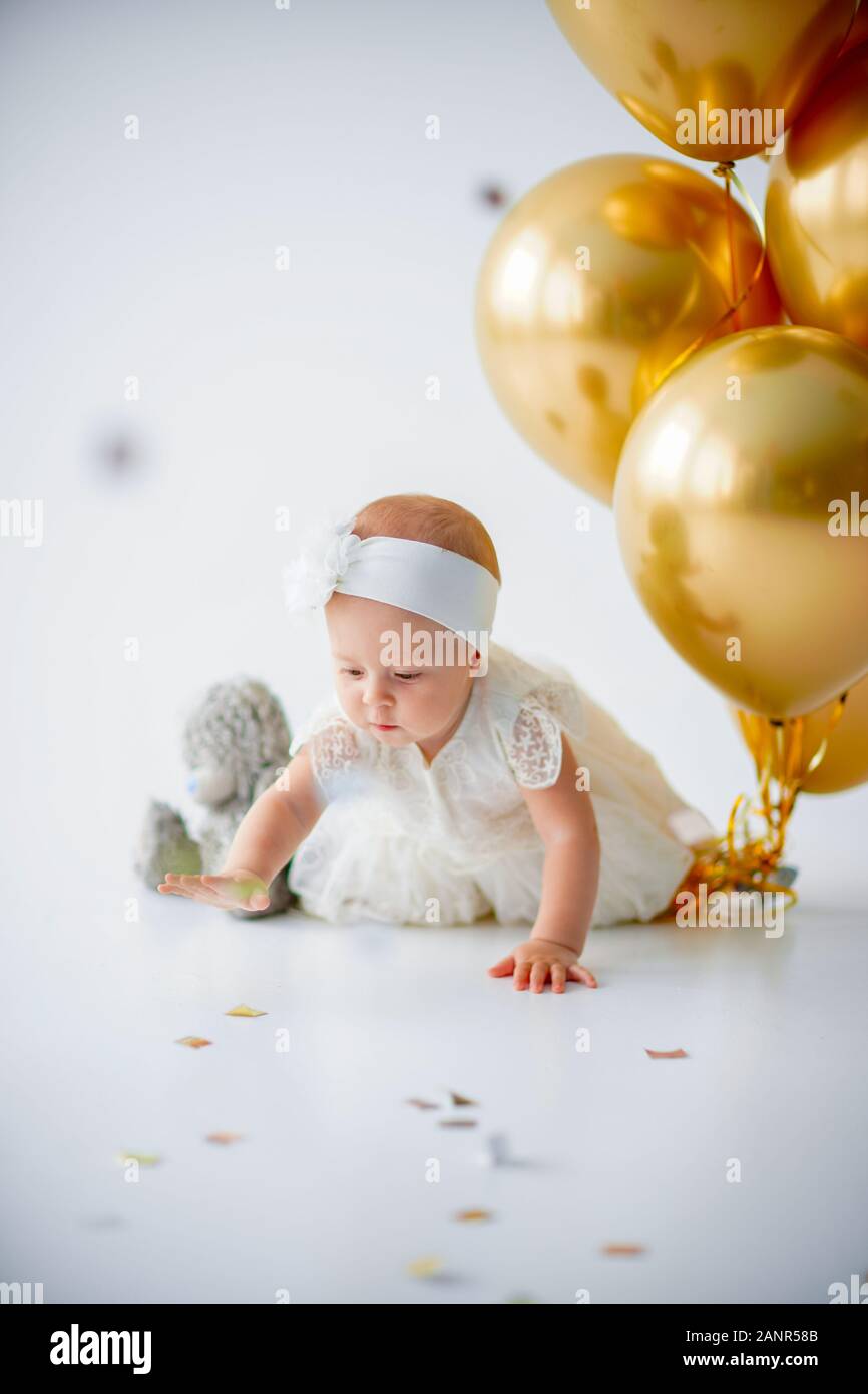 A one year old, baby girl sitting with a bunch of golden balloons ...