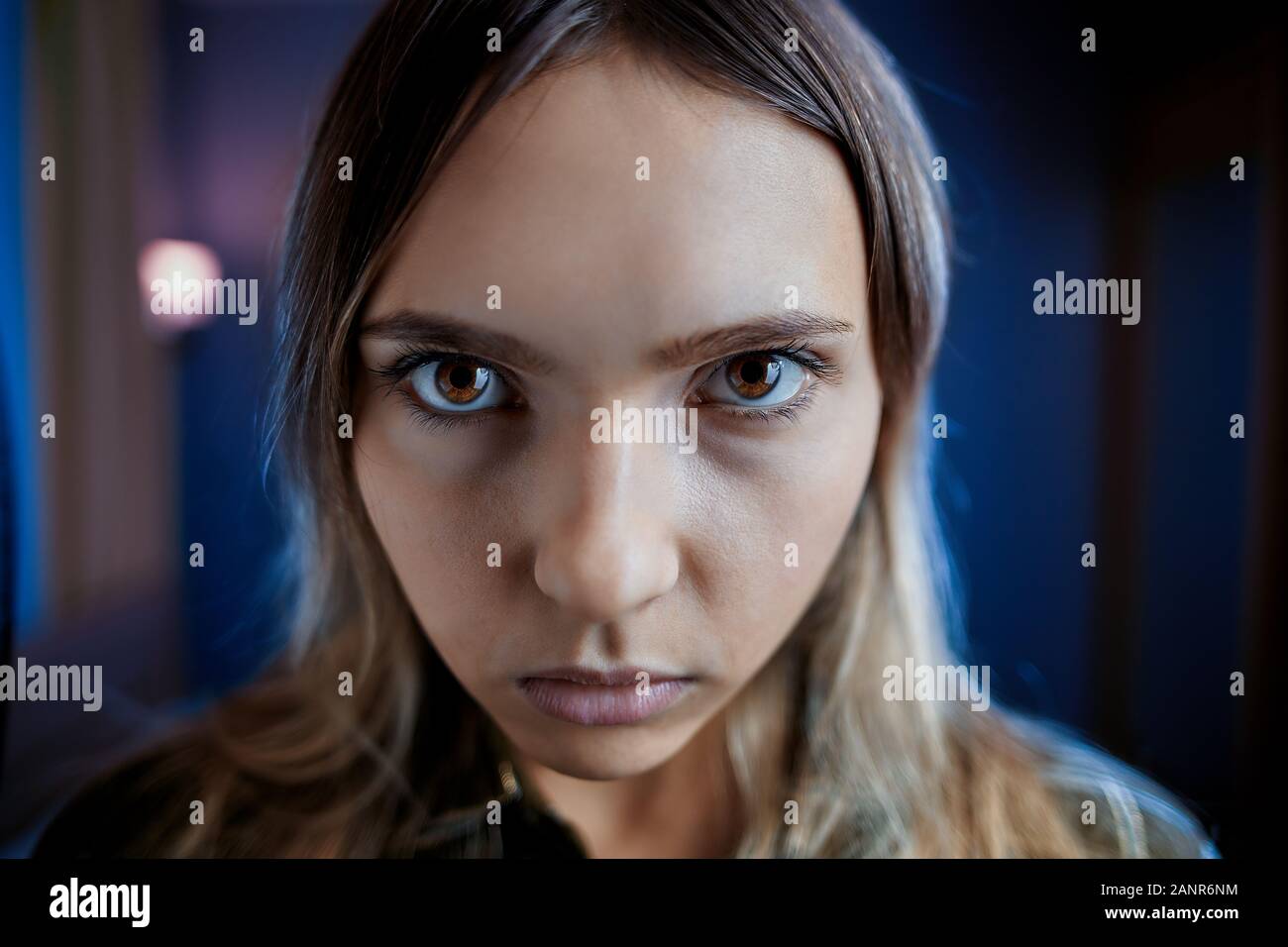 Offended jealous woman with mental disabilities spitefully looks from under her eyebrows. Young paranoid female with a gaze of brown eyes, face close- Stock Photo