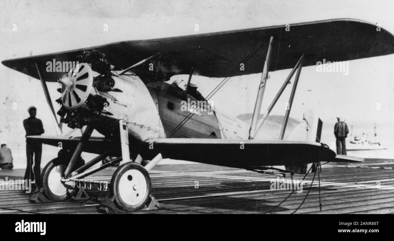 Boeing F2B-1 fighter plane Aboard USS LANGLEY (CV-1), 1928. This photo shows the arresting gear in use at that time. In addition to the usual tail hook, the plane carried a 'comb' arrangement of anchor shaped hooks on its landing gear axle. These engaged a series of fore and aft wires on the carrier's flight deck, preventing the plane from veering to either side. The fore and aft wires can be seen on the deck below the plane. When in use, they were raised off the deck by wooden 'fiddle blocks'. Stock Photo