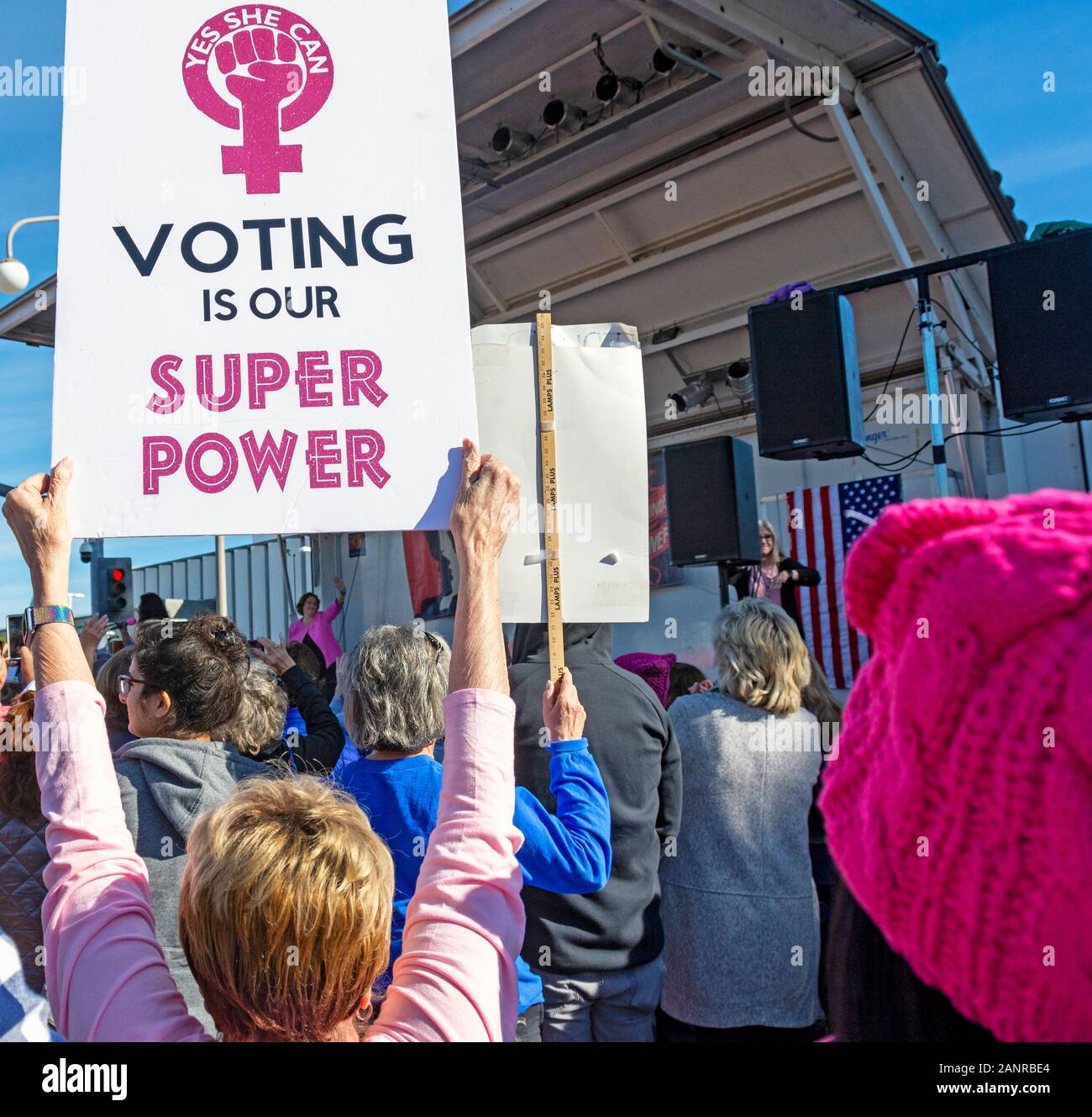 A woman holds a “Voting Is Our Super Power” Woman Power sign at the 2020 OC Women’s March. U.S. Representative Katie Porter is onstage in background. Stock Photo