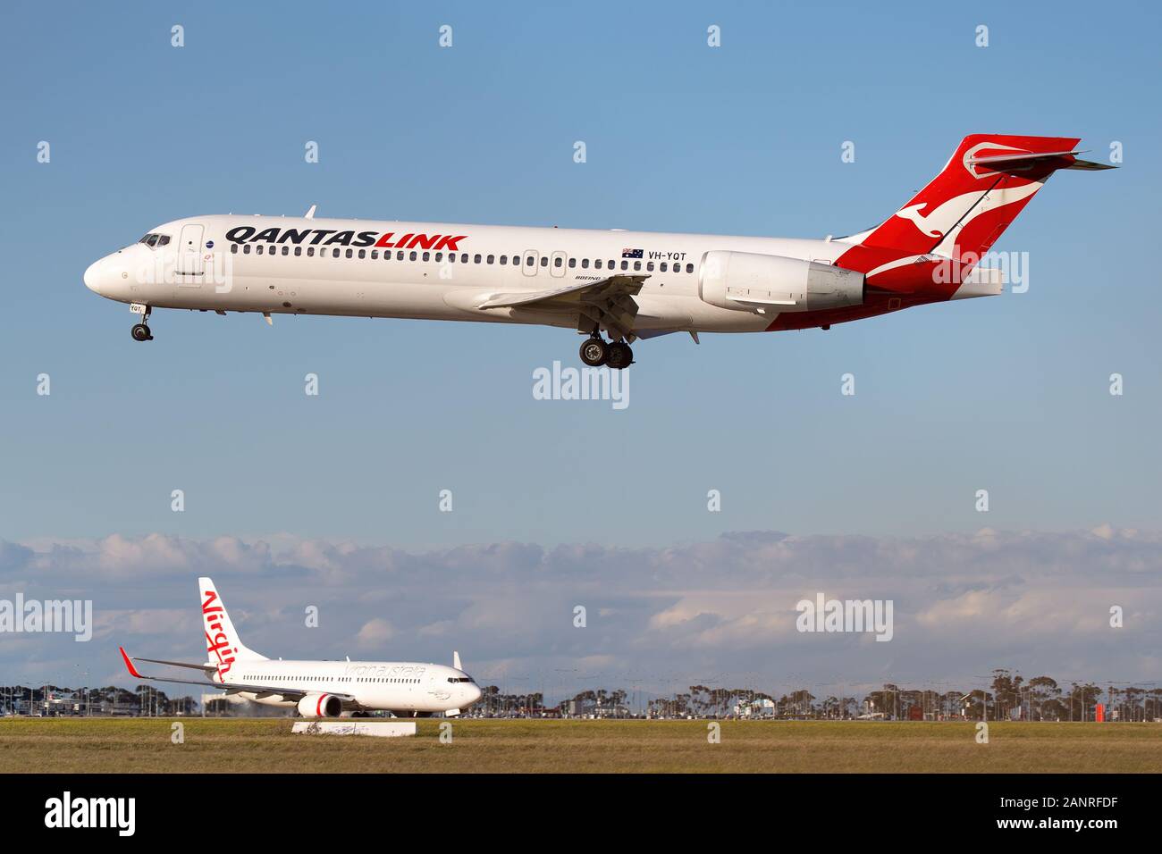 Boeing 717 regional airliner operated by QantasLink on approach to land at Melbourne Airport with a Virgin Boeing 737 taxiing in the background. Stock Photo