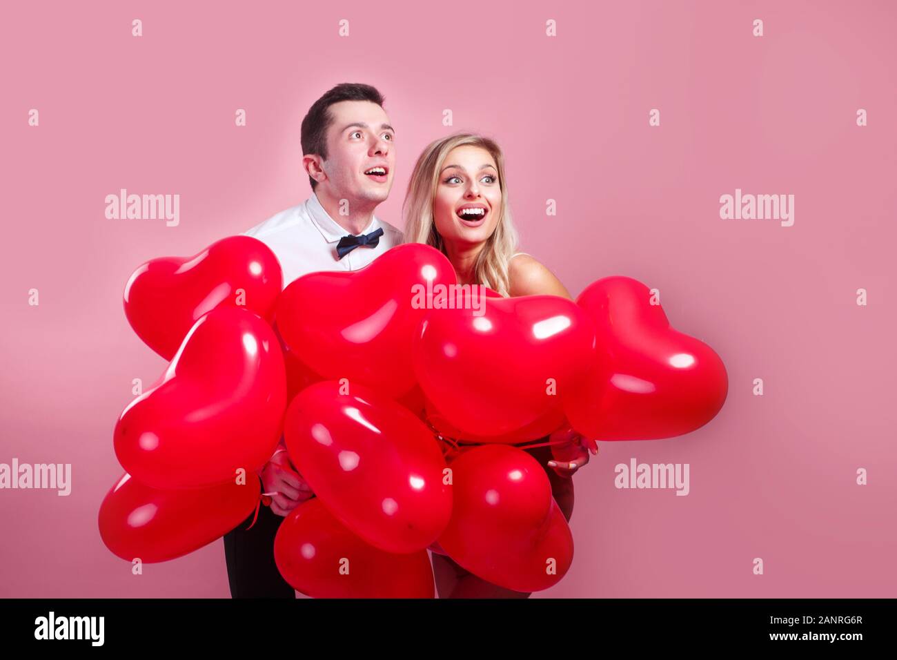 Funny surprised young couple with balloons heart on pink background ...
