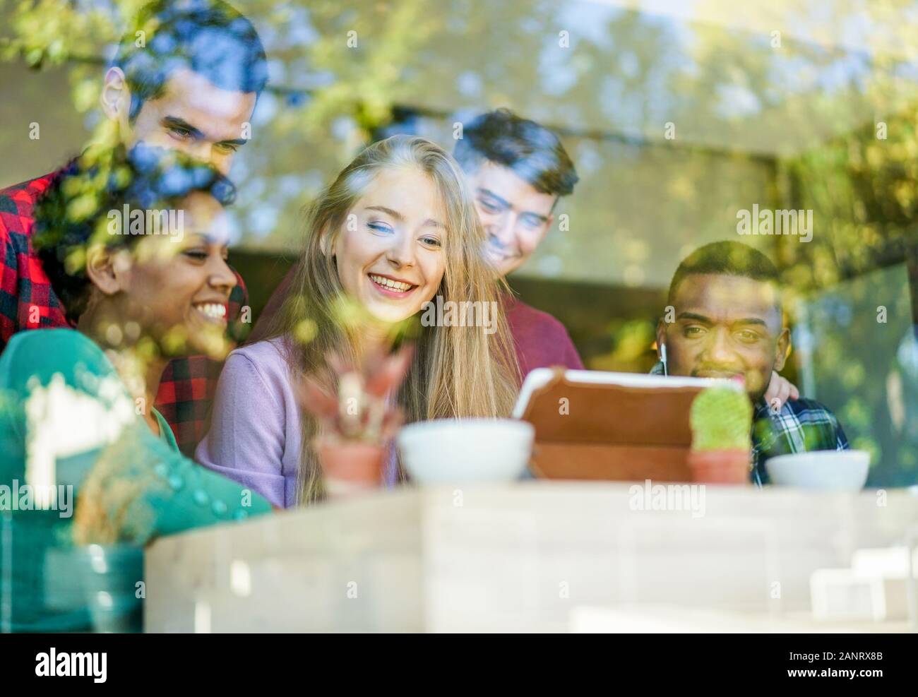 Young cheerful friends drinking coffee and watching together videos on tablet computer - Happy people in bar restaurant having fun with window reflect Stock Photo