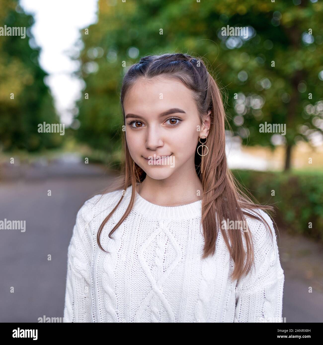 Portrait of a teenager girl 12-15 years old, in summer in city, casual wear white knitted sweater. Happy smiles. The concept of parenting and thoughts Stock Photo